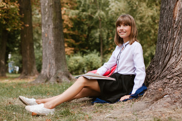 Naklejka na ściany i meble schoolgirl sits under a tree in the park