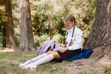 A schoolgirl does lessons in a park under a tree