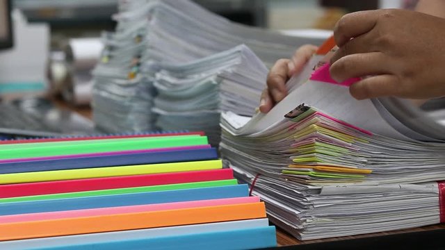 Education and business concept. Asian teacher hands is searching for student's homework assignments archive with colorful papers on table to make a check and inspect. Stack of paperwork and reports. 