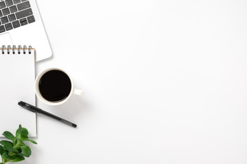 office desk with laptop, coffee cup, pen, blank notepad and green leafs. flat lay with copy space.