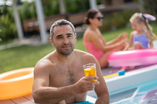 Man drinking cold cocktail while chilling with family near pool