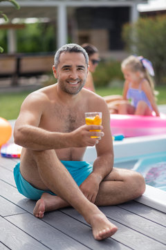Bearded father sitting near pool with his wife and daughter