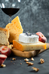 Red wine and cheese. Different types of cheese with nuts, lavander and fig peach on cutting board. Romantic dinner. Copy space for design. Dark background. Soft focus