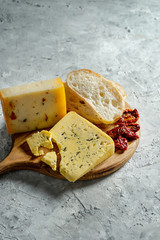 Different types of cheese on wooden cutting board. blue cheese with ciabatta and sun-dried tomatoes on grey background. Italian cuisine dinner. Copy space. Soft focus, close up
