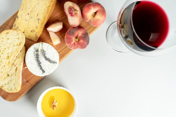 Top view different types of cheeses on wooden cutting board. Cheese with fig peach, honey, ciabatta and nuts, glass of red wine. Stylish food flat lay on grey background. Copy space. Soft focus
