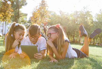 schoolchildren, two girls and a boy enthusiastically watch content on the tablet, actively commenting on what they saw.