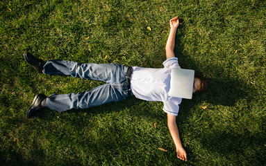 a tired schoolboy lies on the grass and covers his face with a tablet