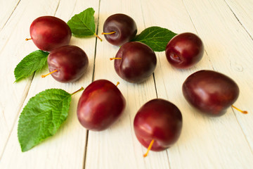 Plums on a white wooden background.Many beautiful plums with leaves.