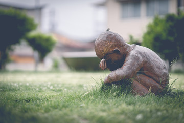 The statue of a little boy is sitting and crying alone in the lawn.