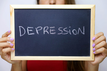 Depression written on the blackboard holding by young unidentified woman.
