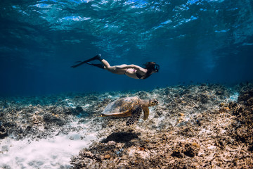 Woman freediver with fins glides underwater near sea turtle.