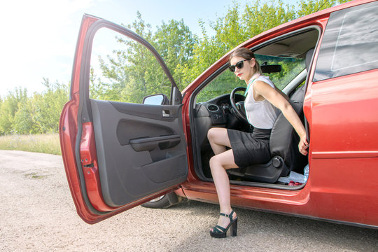 Attractive young woman in office clothes sit in the car, opens the car door.