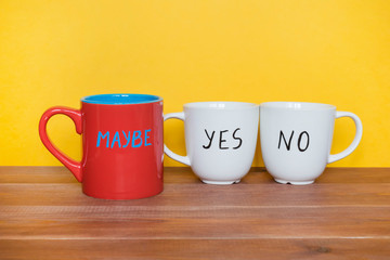 Uncertainty or doubts concept, mugs with words Yes, No and Maybe on the yellow background.