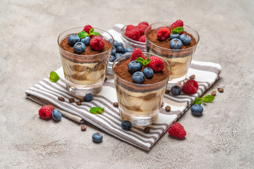 Classic tiramisu dessert with blueberries and raspberries in a glass on kitchen towel on concrete background