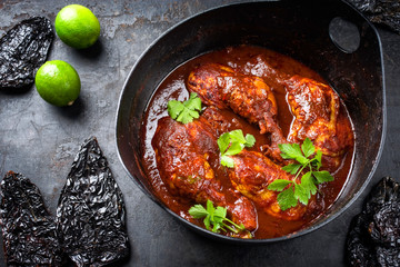 Traditional roasted Mexican pollo adobado chicken haunch with guajillo and hot ancho chilis as closeup in a modern design cast iron stewpot