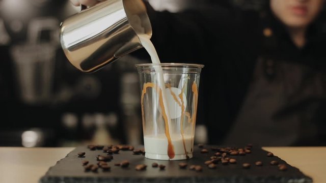 A barista pouring milk into a plastic cup with caramel on the sides. A close-up