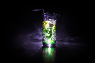 Cocktail glass splashing on dark toned smoky background or colorful cocktail in glass. Party club entertainment. Mixed light.