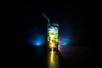 Cocktail glass splashing on dark toned smoky background or colorful cocktail in glass. Party club entertainment. Mixed light.