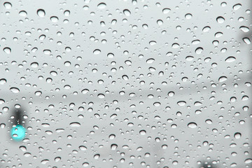 Close up rain drops on car windshield window on blurred green traffic lights background