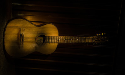 Obraz na płótnie Canvas An wooden acoustic guitar is against a grunge textured wall. The room is dark with a spotlight for your copyspace.
