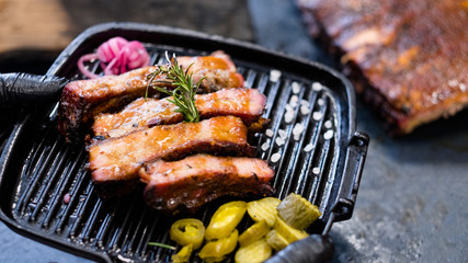 Grilled meat recipe. Smoked pork ribs, served in griddle pan and decorated with rosemary twig.