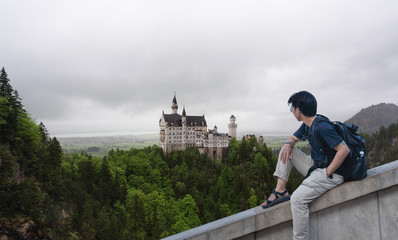 a man with backpack traveling at Neuschwanstein Castle, famous place and travel destination in Fussen, Germany