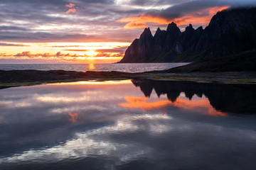 Fototapeta na wymiar Reflection in a rockpool of impressive Oksen Mountain range at very colorful sunset, Tungeneset, Senja, Norway
