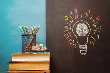 Book, pencils and light bulb with human brain and Hebrew letters on chalkboard