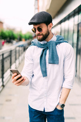 Closeup shot of young man messaging on smartphone. Happy smiling businessamn looking at smart phone leaning against a urban scene.