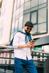 Closeup shot of young man messaging on smartphone. Happy smiling businessamn looking at smart phone leaning against a urban scene.