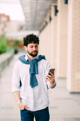 Happy guy having walk in the city and typing sms in the street