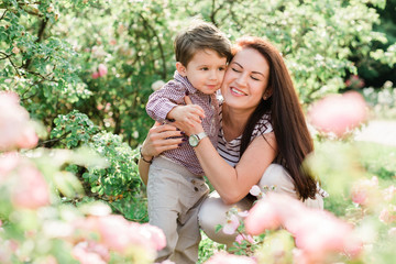 Happy mother with cute little boy having fun outdoors. Cheerful woman playing with her son in park. Joyful motherhood.