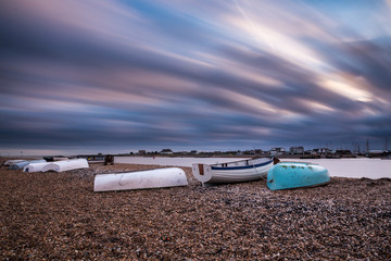 Up turned row boats on a stoney beach in Suffolk. Long streaky clouds from a long exposure