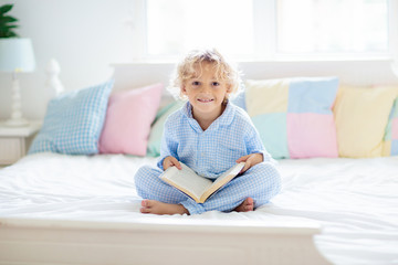 Child reading book in bed. Kids read in bedroom.