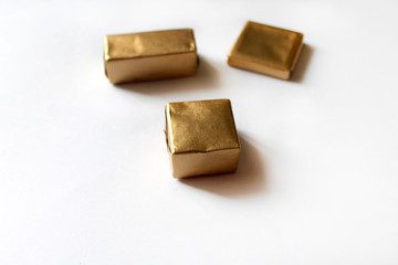 Chocolate candies wrapped in golden foil isolated on white surface. Template for greeting card, poster or invitation. Sweets scattered on white smooth table. Backdrop or background