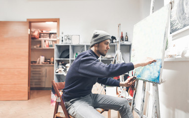 Portrait of a creative young man painting a oil painting at home in a studio. Painting as a hobby and work. Creative business.
