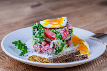 Delicious salad with broccoli, tomato, onion and boiled egg with cream sauce in plate on wooden background. Healthy food
