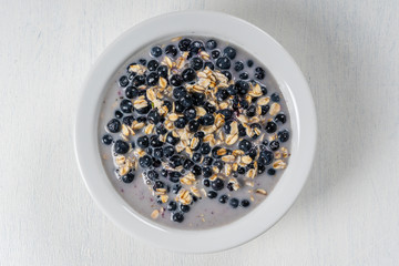 Oatmeal with fresh blueberry, almond milk and honey for breakfast in plate on wooden background. Rustic style. Top view.