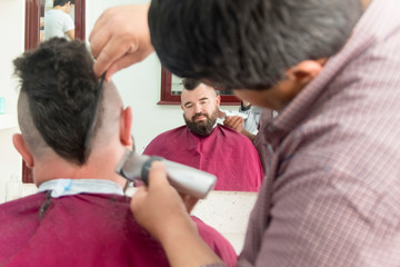 A man with a mohawk and a beard in a barbershop. Hairdresser does a haircut.
