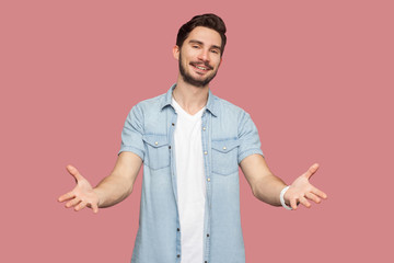 Portrait of happy handsome bearded young man in blue casual style shirt standing with raised arms...