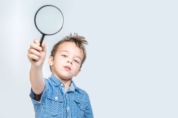 Cute boy holding a magnifying glass on a white background in the studio.