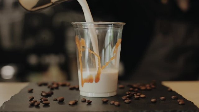 Pouring hot milk into a takeaway plastic glass with caramel on the walls. Close-up