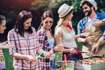 Young friends having fun grilling meat enjoying barbecue party.