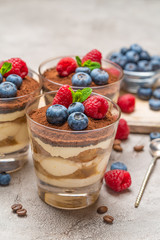 Classic tiramisu dessert with blueberries and raspberries in a glass and bowls with berries on concrete background