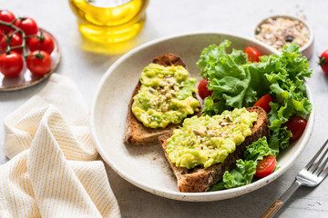 Mashed avocado cream with seeds and green salad of kale, olive oil and cherry tomatoes on plate. Healthy lunch, breakfast. Clean eating concept, vegetarian vegan food