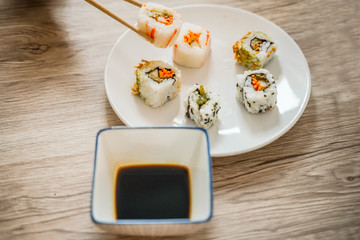 Chopsticks taking portion of sushi roll on the wooden table restaurant / eating sushi roll using chopsticks- Image