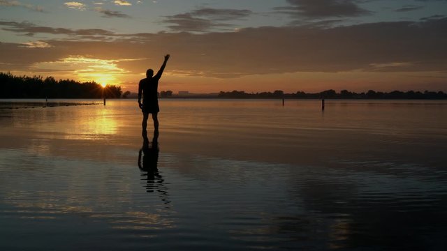 sunrise silhouette of a senior man standing in shallow water and  practicing chigong breathing and movements, Boyd Lake State Park in northern Colorado