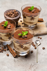 Classic tiramisu dessert in a glass and cinnamon sticks on concrete background