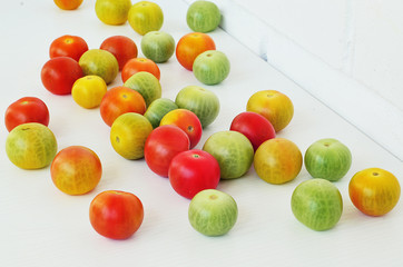 Red, green and yellow tomatoes on white background. Tomatoes of different colors and varieties. Juicy tomatoes on a white table. Colorful vegetables.