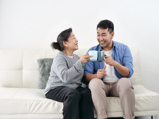 Asian mother and her son talking and drinking at home, lifestyle concept.